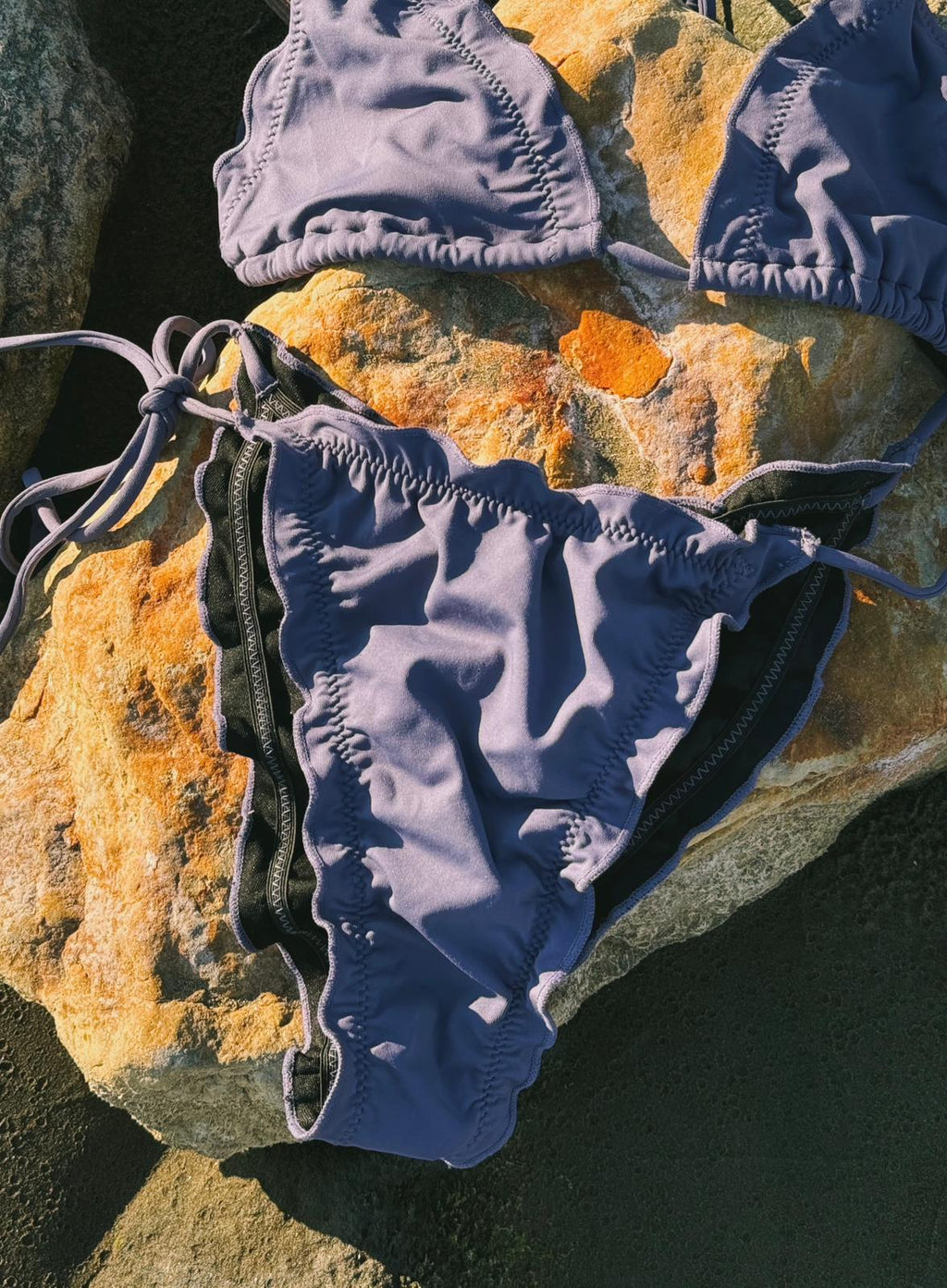 Ornella Purple bikini set on an orange rock by the beach