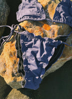 Ornella Purple bikini set on an orange rock by the beach